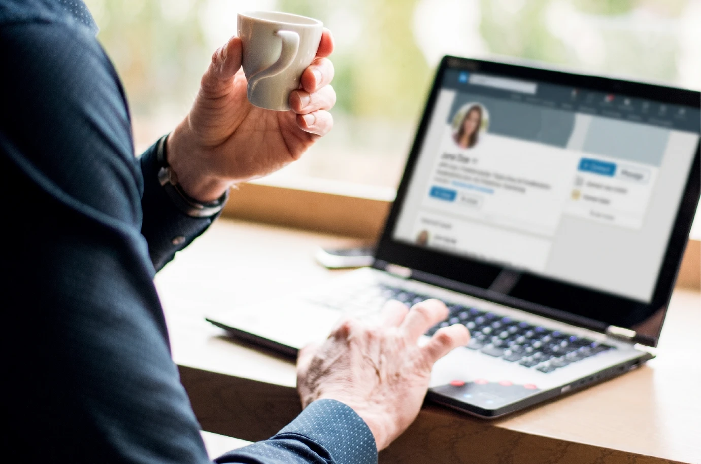 Persona revisando perfil de LinkedIn en laptop con taza de café en mano